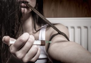 Drug addict young woman with syringe in action